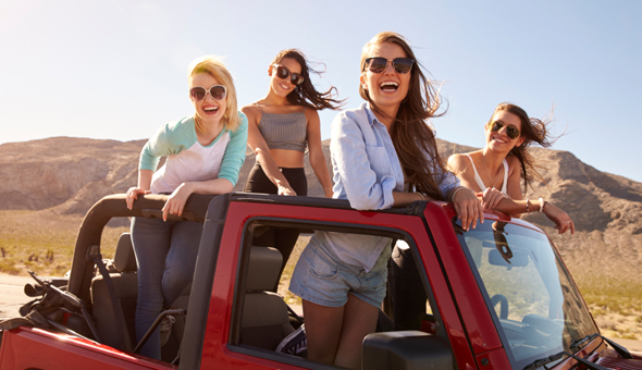Four Female Friends On Road Trip Standing In Convertible Car